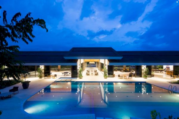 A luxurious poolside resort illuminated at dusk, featuring a large swimming pool, comfortable seating areas, and a spacious open-air pavilion.