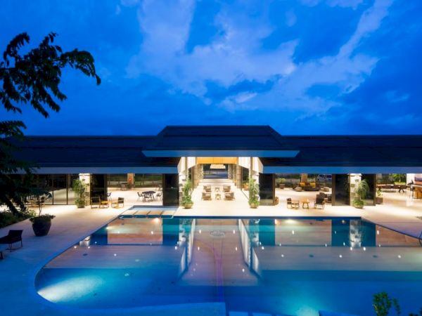A luxurious poolside resort illuminated at dusk, featuring a large swimming pool, comfortable seating areas, and a spacious open-air pavilion.