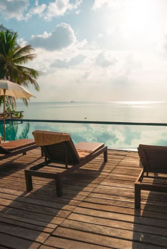 This image shows a serene poolside area with lounge chairs, umbrellas, and a view of the ocean under a partly cloudy sky.