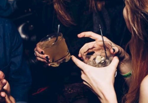 People are socializing, laughing, and holding drinks in a dimly lit setting, possibly a bar or a party, with a lively atmosphere.