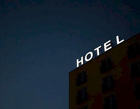 The image shows the top portion of a building against a dark sky with the word "HOTEL" in illuminated letters.