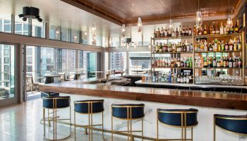 A modern bar with a sleek design, featuring a well-stocked liquor shelf, bar stools, and large windows offering a cityscape view, ending the sentence.