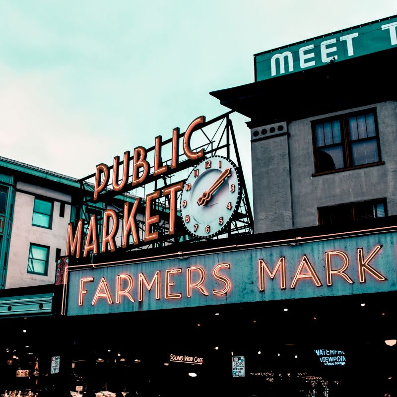 This image shows an iconic farmers market, with a neon sign that reads "Public Market" and "Farmers Market," and a clock on the building.
