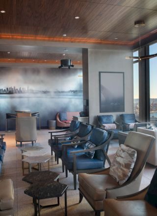A modern lounge with comfortable seating, large windows offering a scenic view of a waterfront and Ferris wheel, and a mural on one wall.