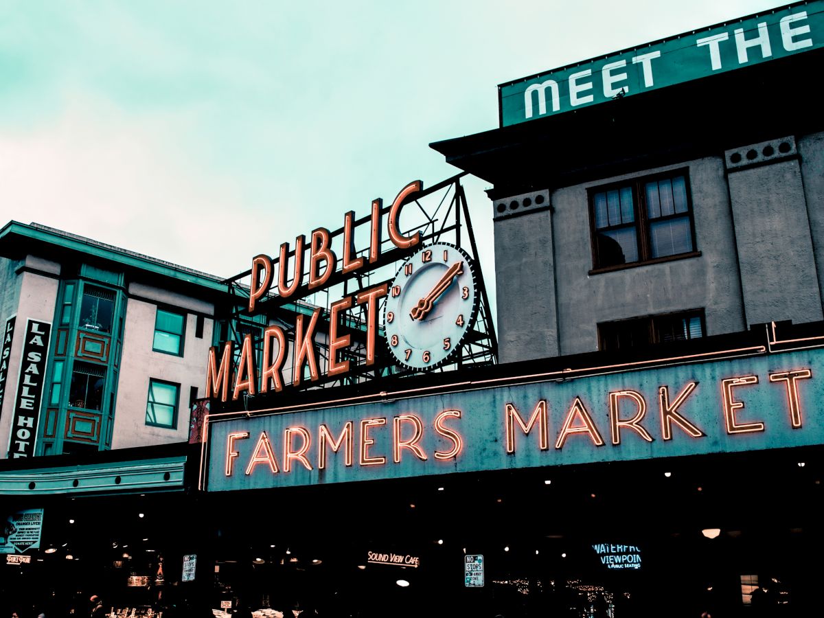 This image shows a famous neon sign reading "Public Market" and "Farmers Market" with a clock in between, located in an urban setting.