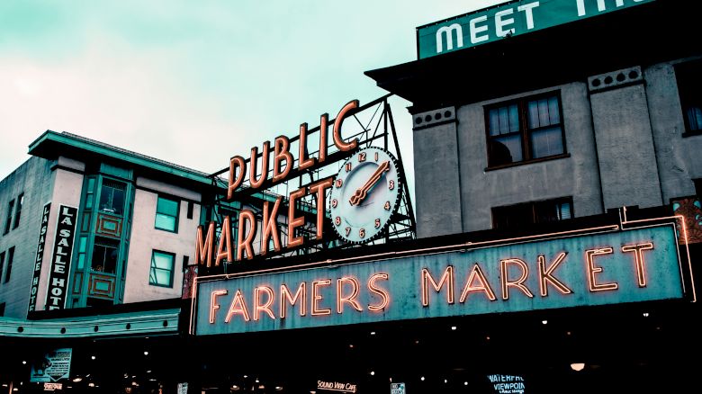 This image shows a famous neon sign reading "Public Market" and "Farmers Market" with a clock in between, located in an urban setting.